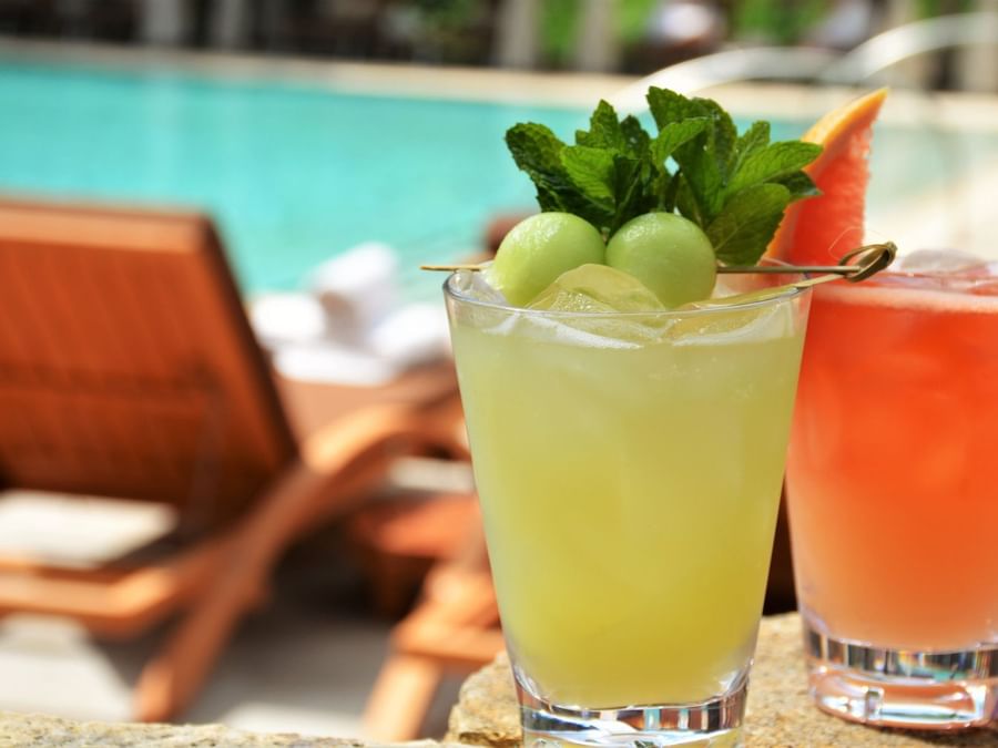 Two refreshing drinks with fruit & garnishes on a table by a pool at The Umstead Hotel and Spa