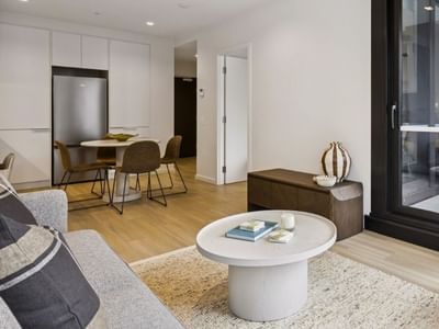 Modern living room with gray couch, round table, and sliding glass door at West Tower, Melbourne Quarter.