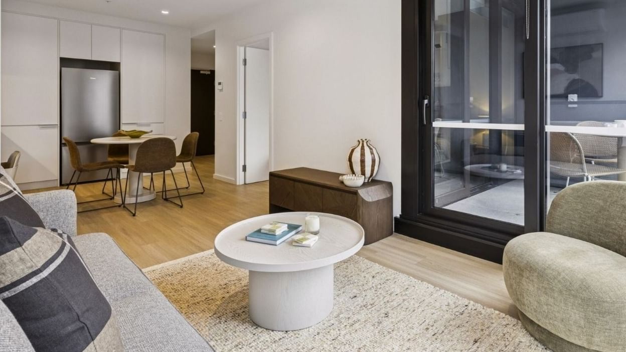 Modern living room with gray couch, round table, and sliding glass door at West Tower, Melbourne Quarter.