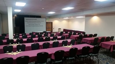 Spacious meeting room at Moab Valley Inn with maroon tables, black chairs, and a screen for presentations