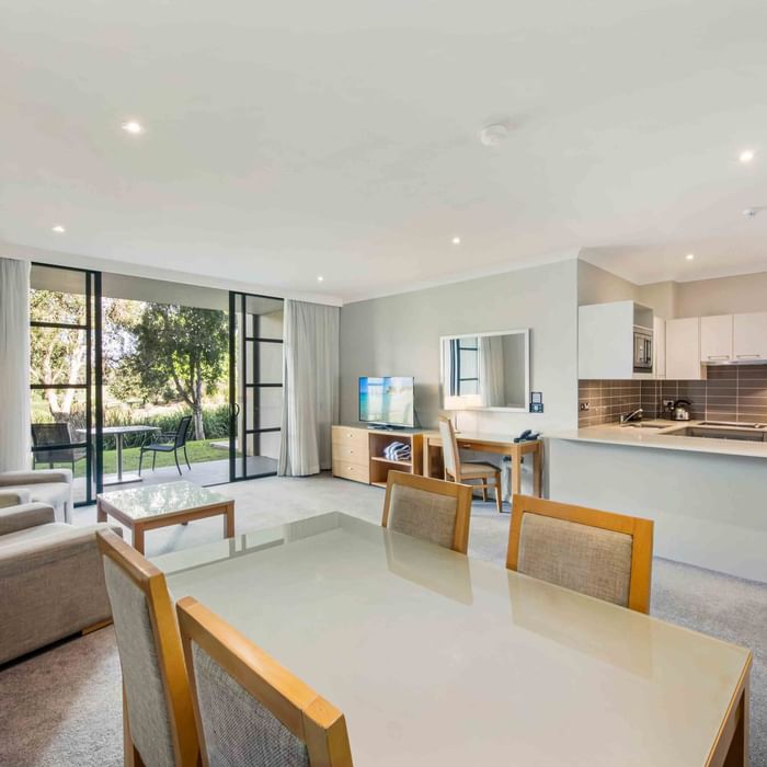 One Bedroom Apartment living room with adjoining kitchen, windows, and sliding door to garden at Mercure Kooindah Waters