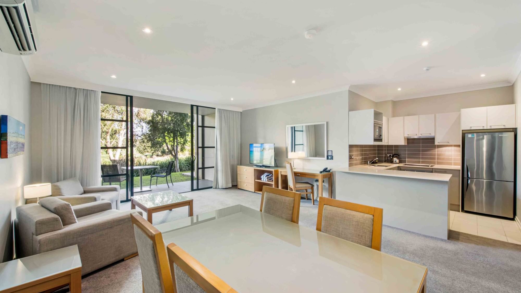 One Bedroom Apartment living room with adjoining kitchen, windows, and sliding door to garden at Mercure Kooindah Waters