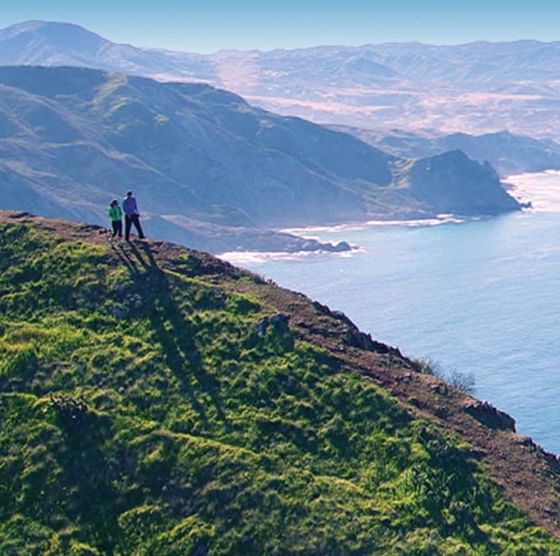 Two people standing on a coastal cliff overlooking the sea and hills nea