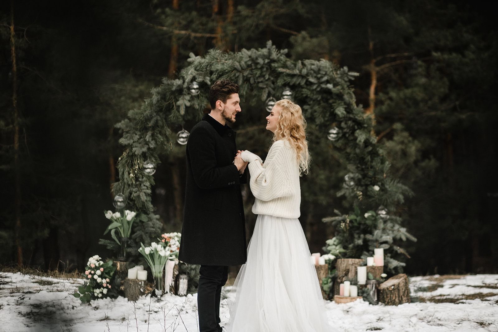 Couple stands holding hands in a snowy forest with a decorated arch and candles at Mountain View Grand Resort & Spa