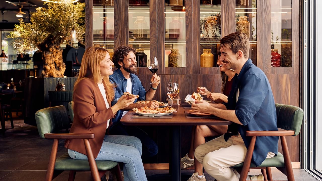 Three guests enjoying wine and appetizers at a modern restaurant table with warm ambient lighting and elegant decor.
