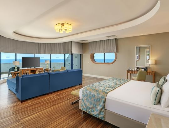 Titanic Deluxe Lara – Admiral Suite’te deniz manzaralı, mavi kanepeli ve beyaz yataklı oda.