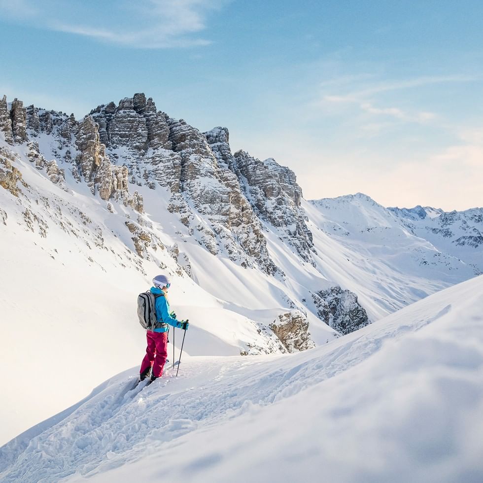 Skifahrerin mit Rucksack und Stöcken auf schneebedecktem Berg in der Sonne.