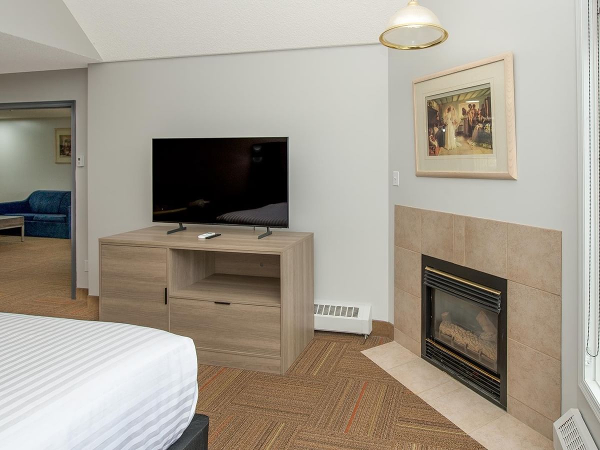 Coast Suite with white bed, flat-screen TV, stone fireplace, and adjoining living area.
