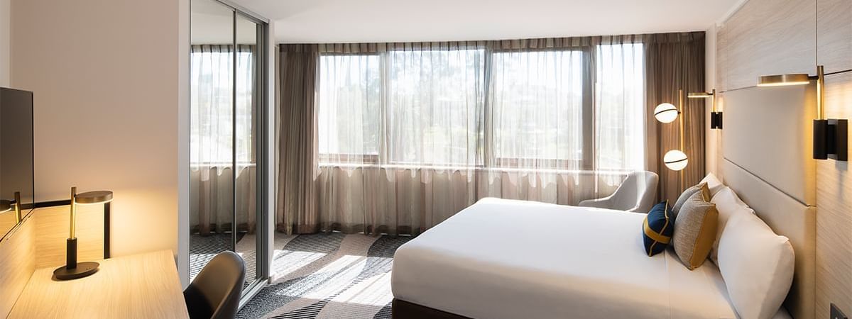 Bed in Superior King Room at Novotel Sydney Parramatta, under globe lights, surrounded by a desk and a large window
