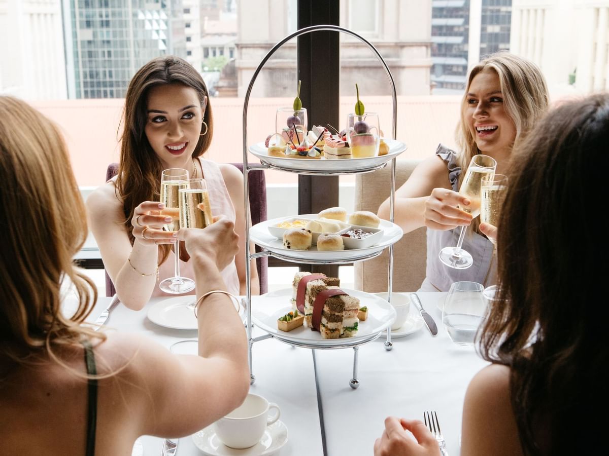 Three people toasting with champagne at a table with a tiered serving tray of desserts at Sofitel Brisbane Central