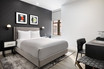 Modern hotel bedroom with gray bed and white pillows, artwork on wall, and black desk at ArtHouse Hotel New York City