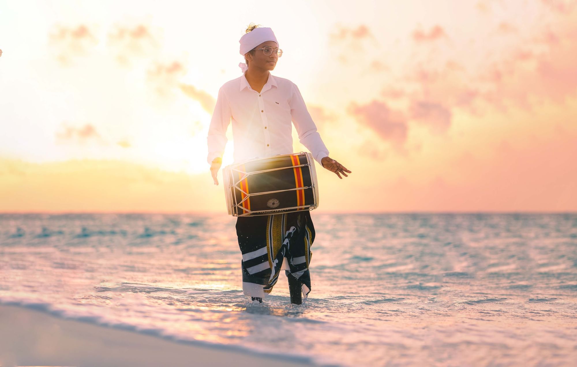 A man playing a drum on a beach near The Signature Collection