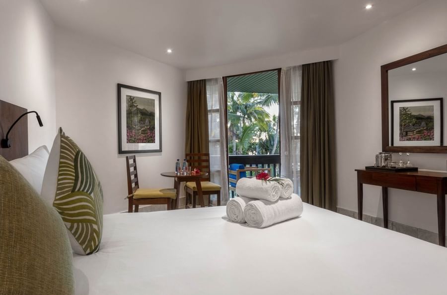 White bed by a round table under a framed art piece near a balcony in Warwick Deluxe Rooms at Warwick Fiji Resort and Spa