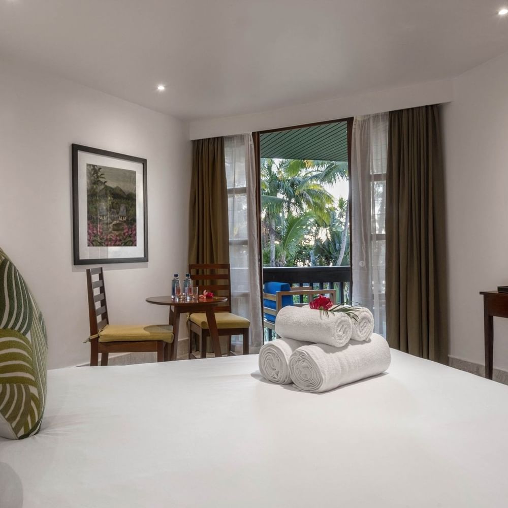 White bed by a round table under a framed art piece near a balcony in Warwick Deluxe Rooms at Warwick Fiji Resort and Spa