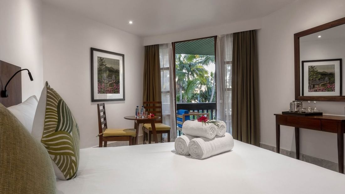 White bed by a round table under a framed art piece near a balcony in Warwick Deluxe Rooms at Warwick Fiji Resort and Spa