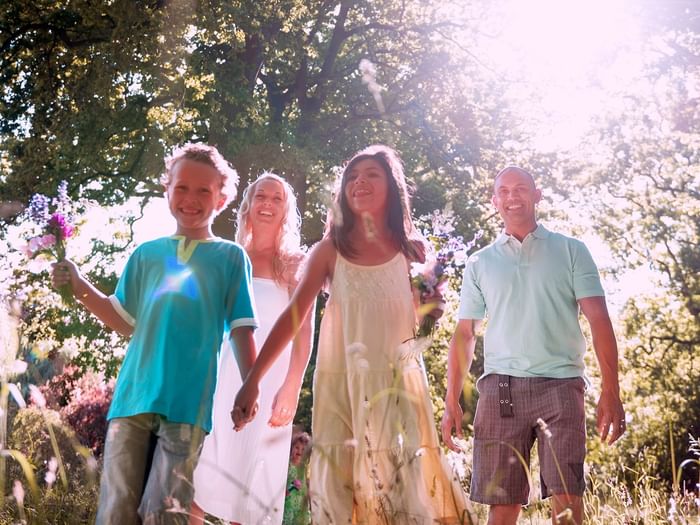 A family of four smiling and walking through a grassy field with sunlight beaming down.