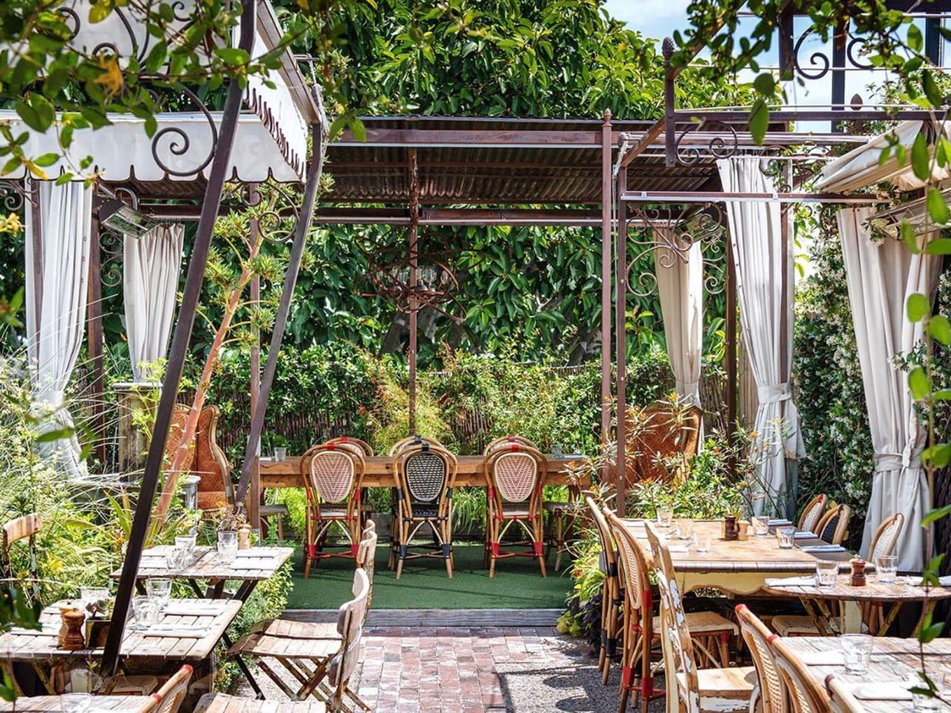 Elegant Gardens patio featuring wooden tables and wicker chairs under a pergola at Petit Ermitage