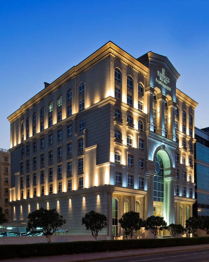 Classic Warwick Doha Hotel exterior with lit windows by a large glass arch at night