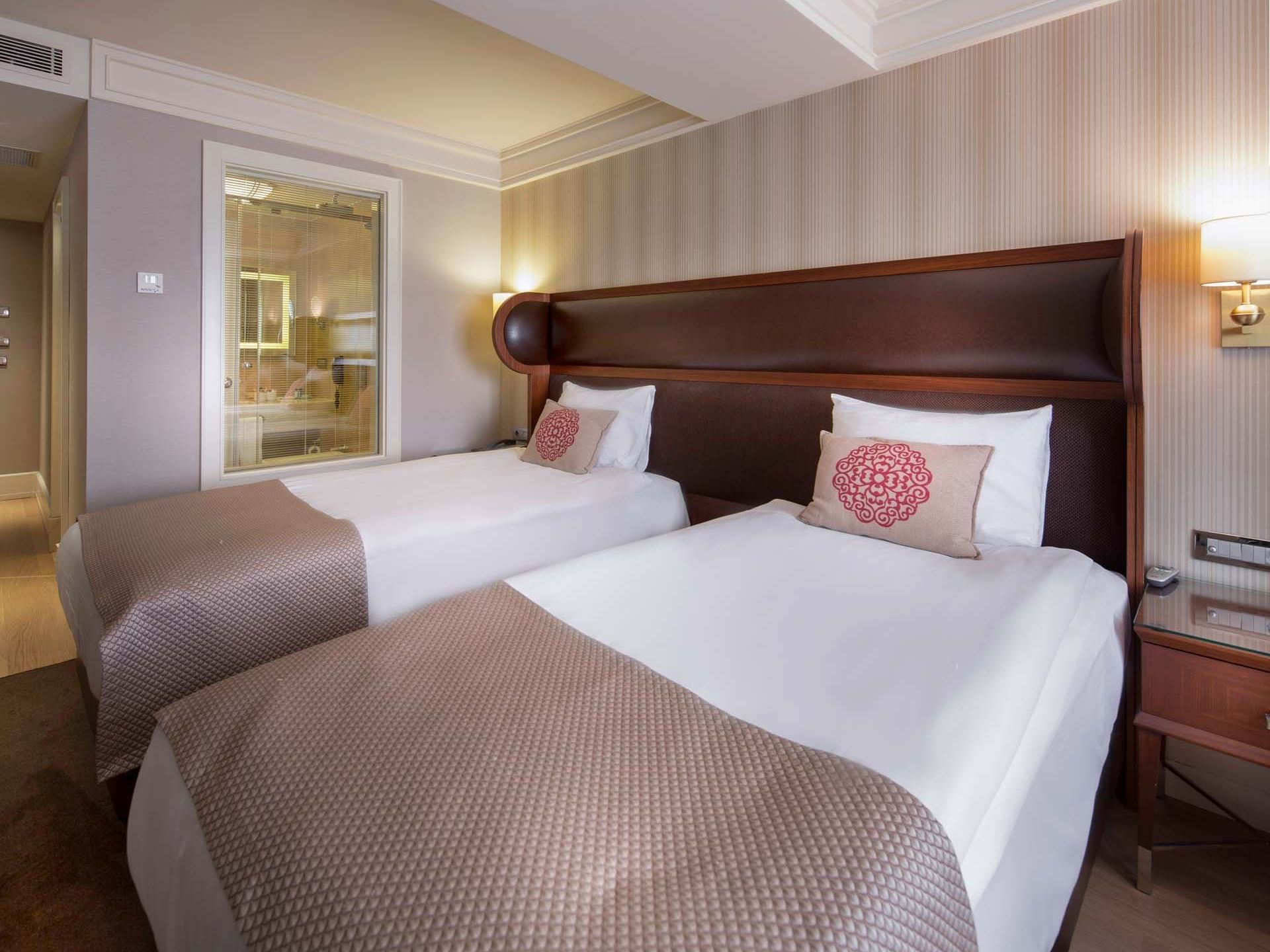 Twin beds arranged in Family Room with a view of the bathroom through a glass at Titanic Comfort Sisli