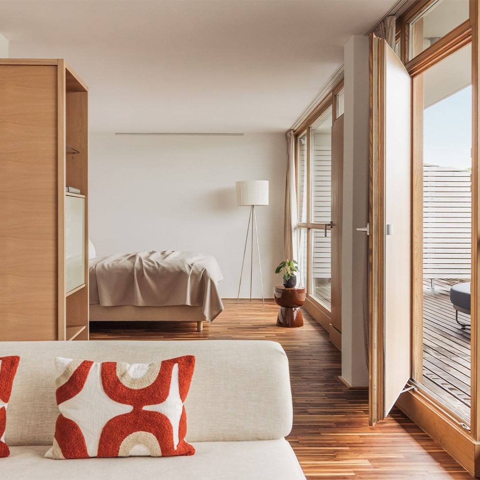 Gemütliches Zimmer mit Bett, Couch, Holzboden, und Balkonzugang durch eine Glastür.