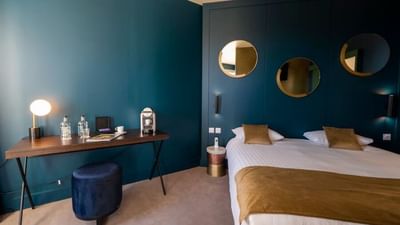 Modern bedroom with teal walls, bed, desk, and three circular mirrors on a blue cabinet.