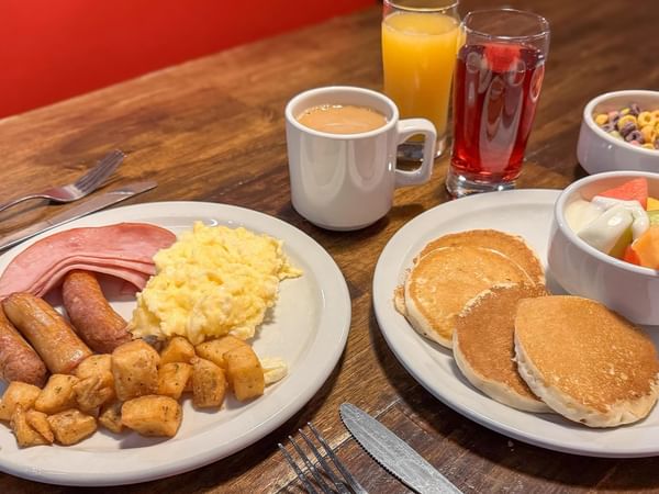 Two plates with breakfast food, coffee, and fruit juice.