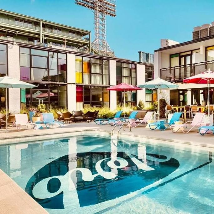 Outdoor pool with colorful umbrellas and lounge chairs beneath a stadium light tower at a modern boutique hotel in Fenway.