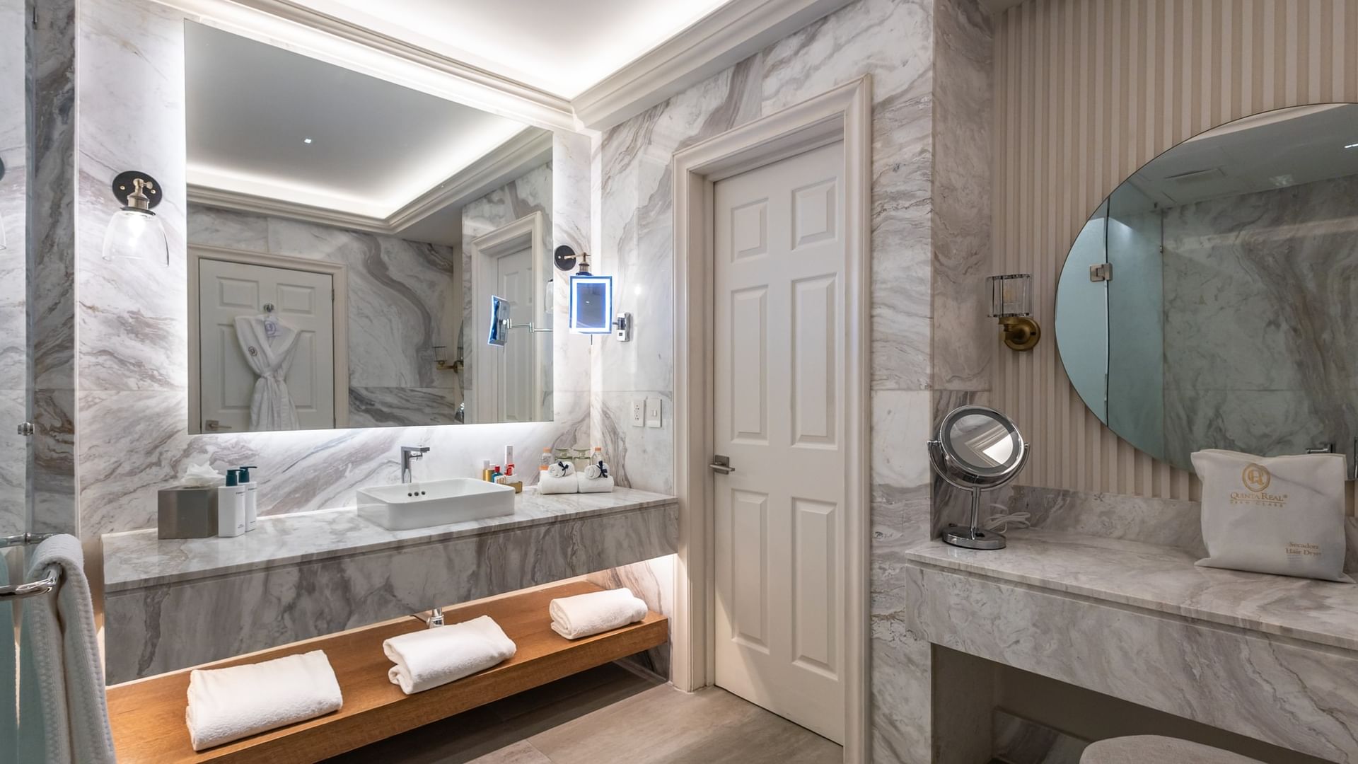Elegant marble bathroom with double vanity, illuminated mirrors, and wooden towel shelf at Quinta Real Monterrey.