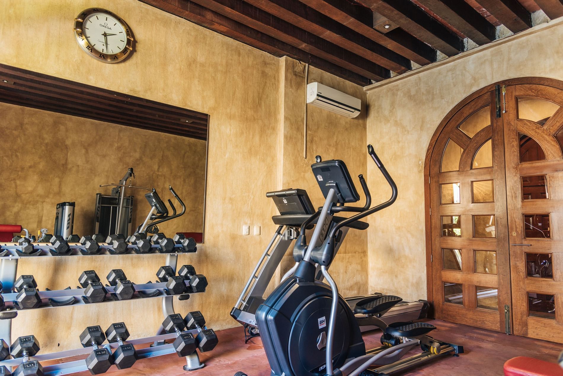 Modern gym with warm-toned walls, featuring a treadmill, elliptical, and a rack of dumbbells at Quinta Real Oaxaca