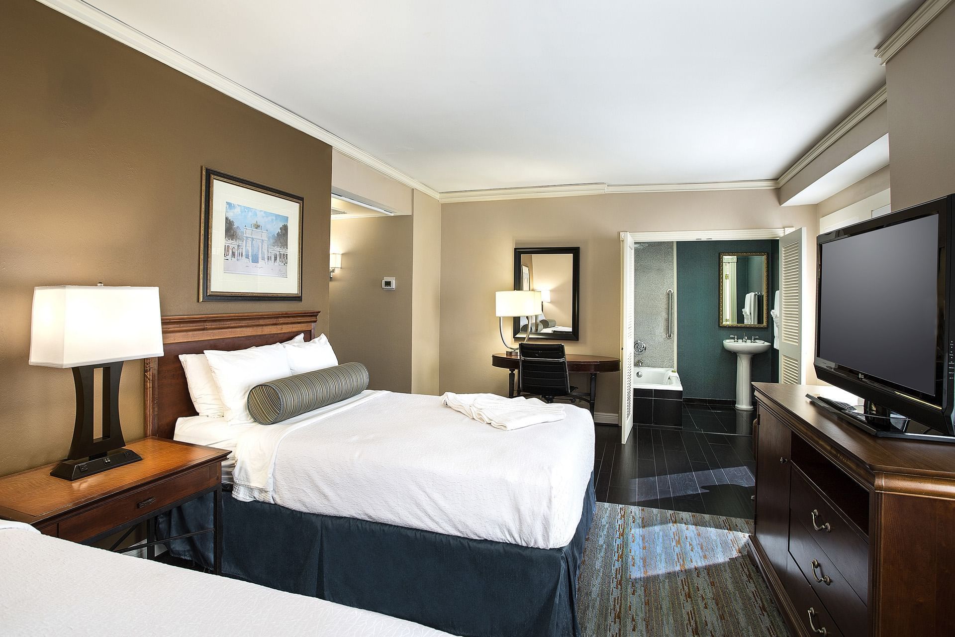 A hotel room with a bed, nightstand, TV, and bathroom in the background.