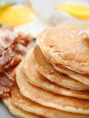Stack of pancakes by crispy bacon and fried eggs under a pat of butter at Warwick San Francisco