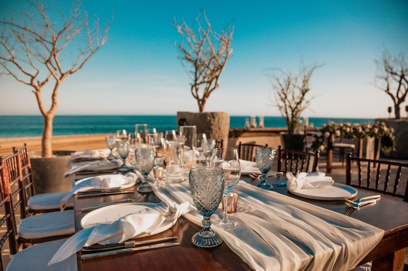 Mesa de comedor al aire libre elegantemente dispuesta con vista al océano.