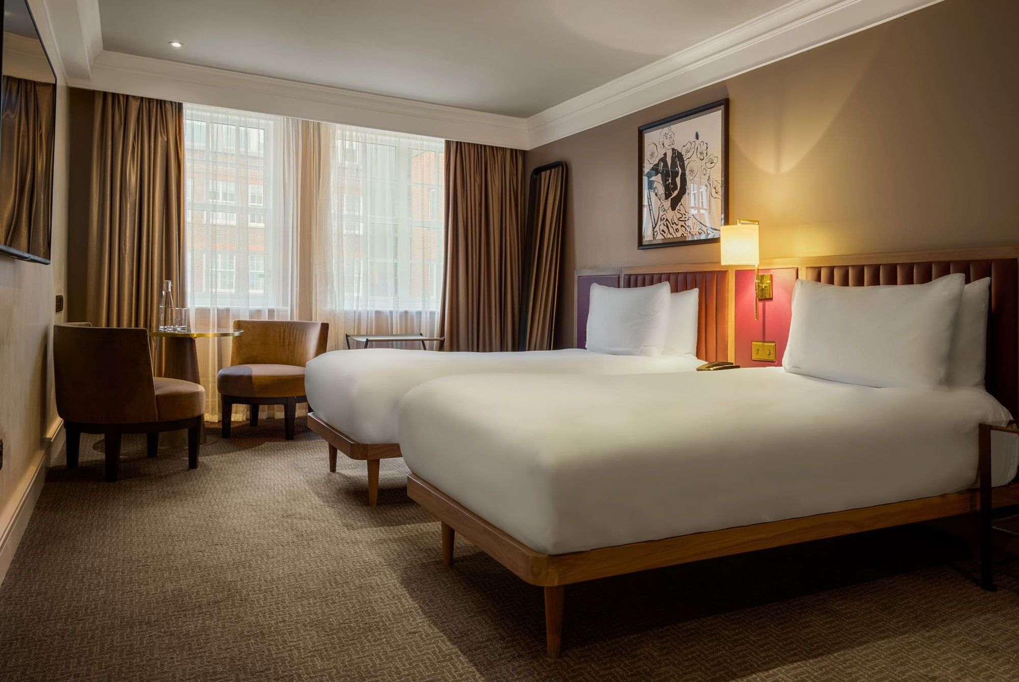 A well-furnished hotel room with two beds, lamps, and a window in London.