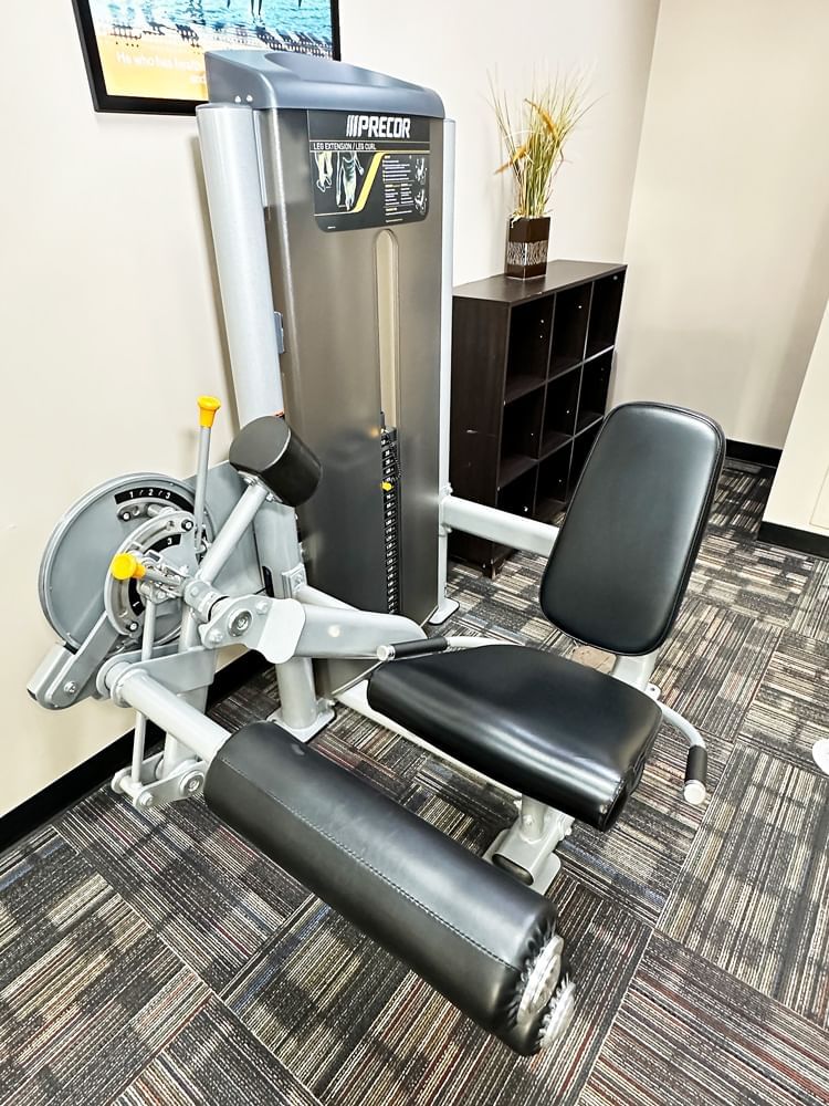 A leg extension machine sits in front of a cubby storage unit and a plant in a gym.