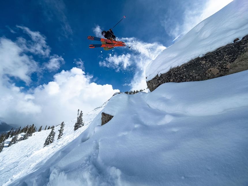 Skier in mid-air with snow splashes near mountain cliff at Elevation Resort & Spa.