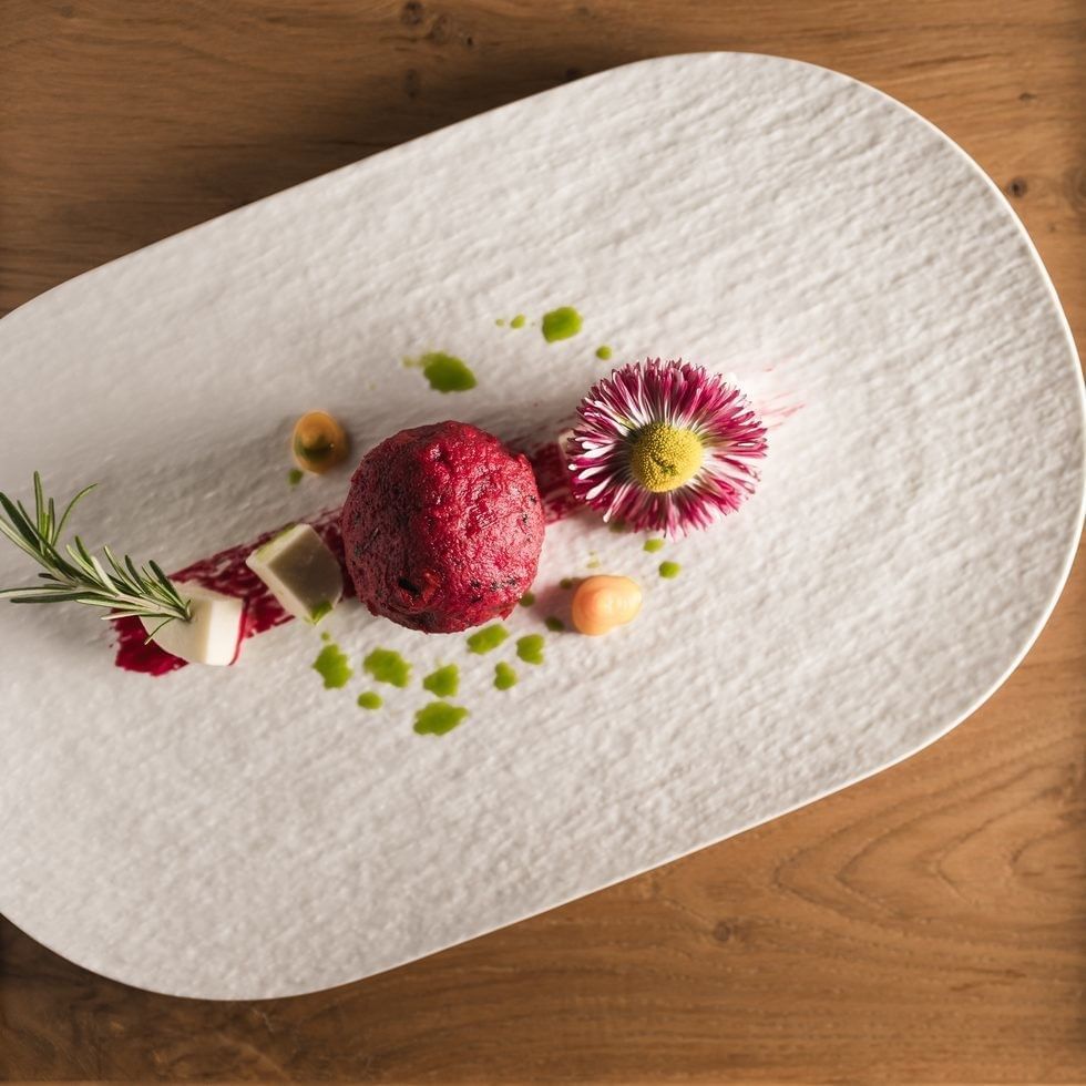 Elegant dish with beetroot, herbs, and flower on a white plate for a cooking class.