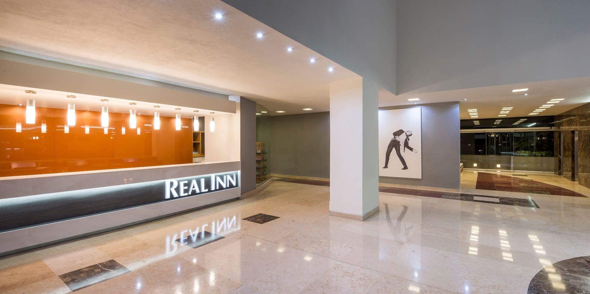 Recepción moderna con pared naranja vibrante y luces modernas en Real Inn San Luis Potosí