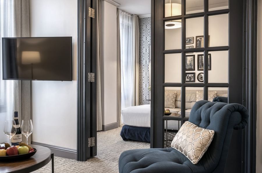 Teal armchair by a glass-paned door opening into a bedroom area in Accessible Executive Front Suite at Warwick San Francisco