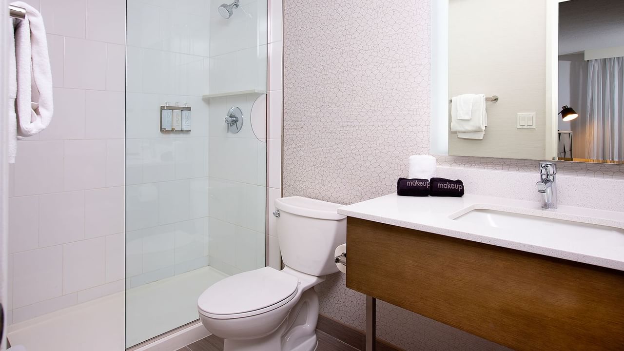White toilet, clear glass shower, and vanity with mirror and sink in a bathroom.