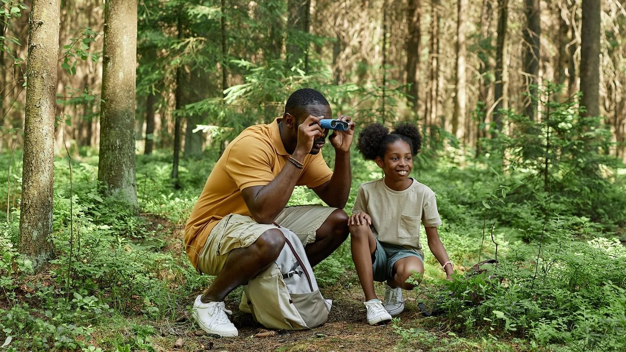 Dad and daughter using binoculars while on a hike. 
