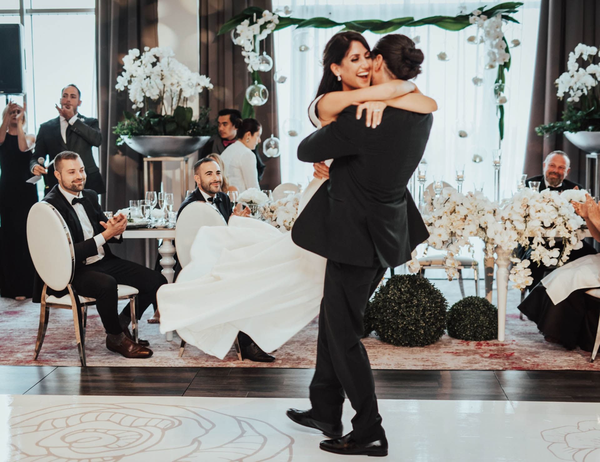 Groom lifting bride on the dance floor during a stylish wedding reception with white flowers at Hotel X Toronto