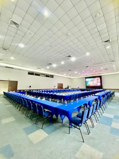 Ritz Meeting Room set with long tables and chairs, featuring a large screen for presentations at Dann Carlton Cali