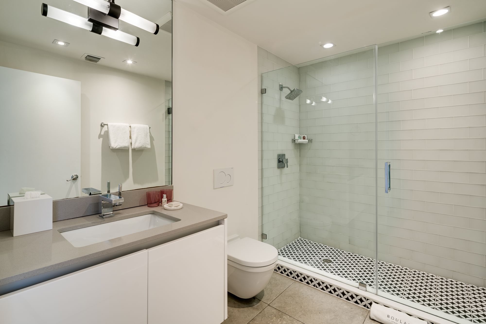 A modern bathroom with a shower, toilet, sink, and mirror.
