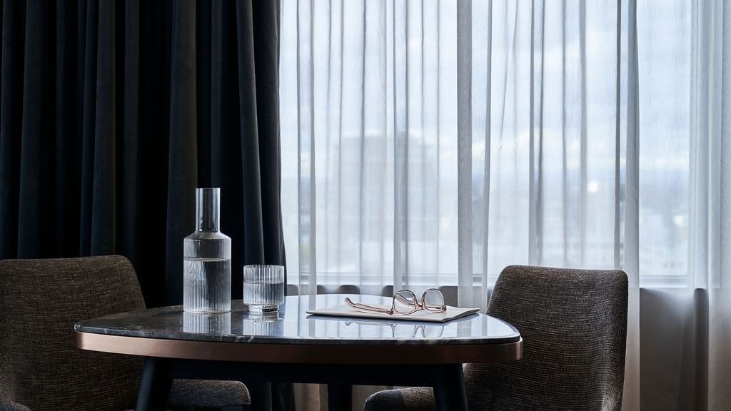 Modern round table with water carafe, glasses, and reading glasses in a Superior Suite at Pullman East Melbourne