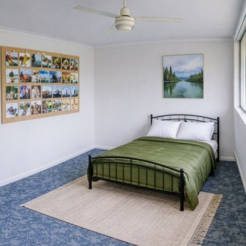 Green bed with white pillows in a room with large windows and a ceiling fan.