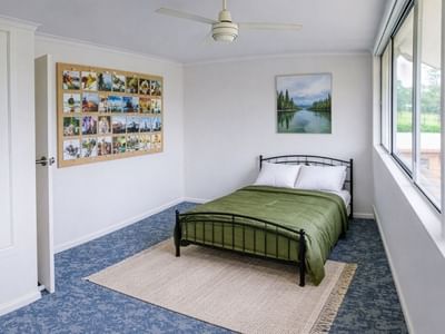 Green bed with white pillows in a room with large windows and a ceiling fan.