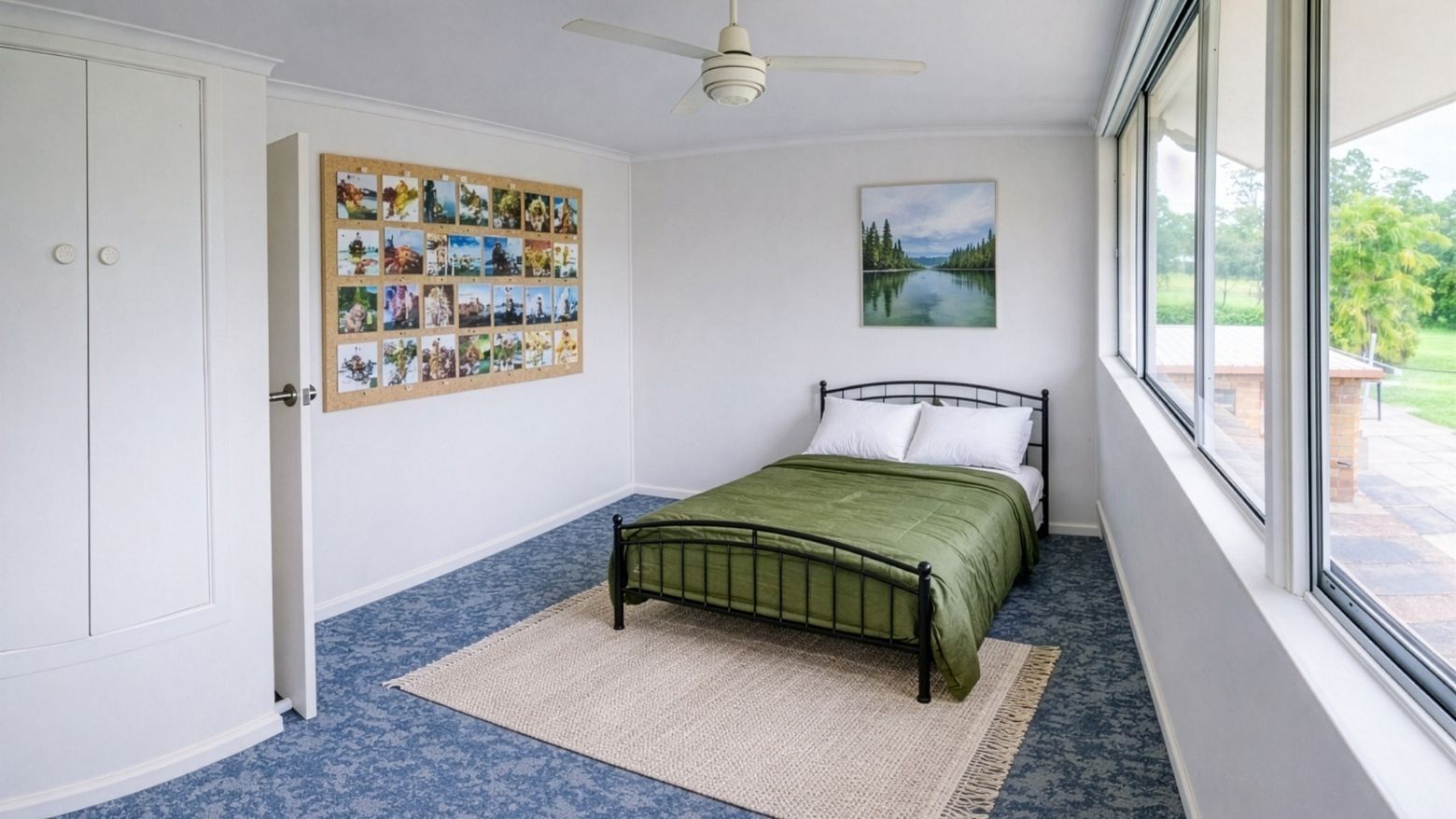Green bed with white pillows in a room with large windows and a ceiling fan.