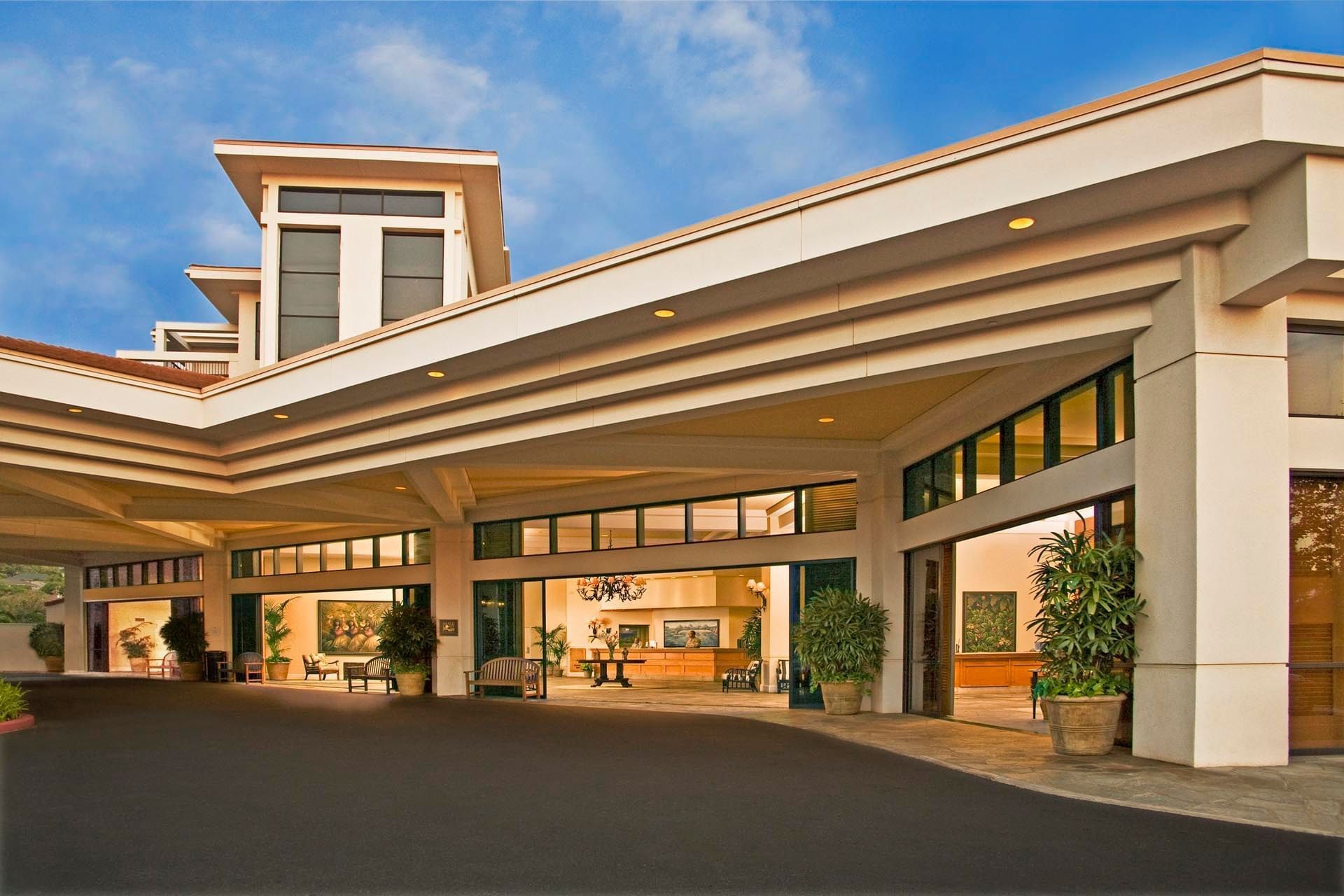 The exterior of a large building with a large overhang and multiple levels, featuring potted plants and a prominent entrance.