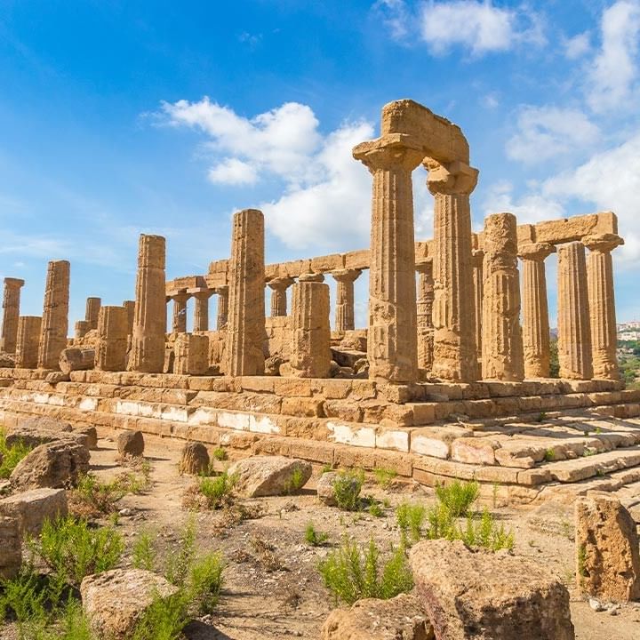 Ruinen eines antiken Tempels auf einem Hügel unter einem blauen Himmel mit weißen Wolken.