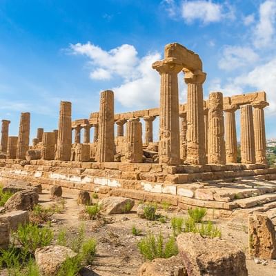 Ruinen eines antiken Tempels auf einem Hügel unter einem blauen Himmel mit weißen Wolken.